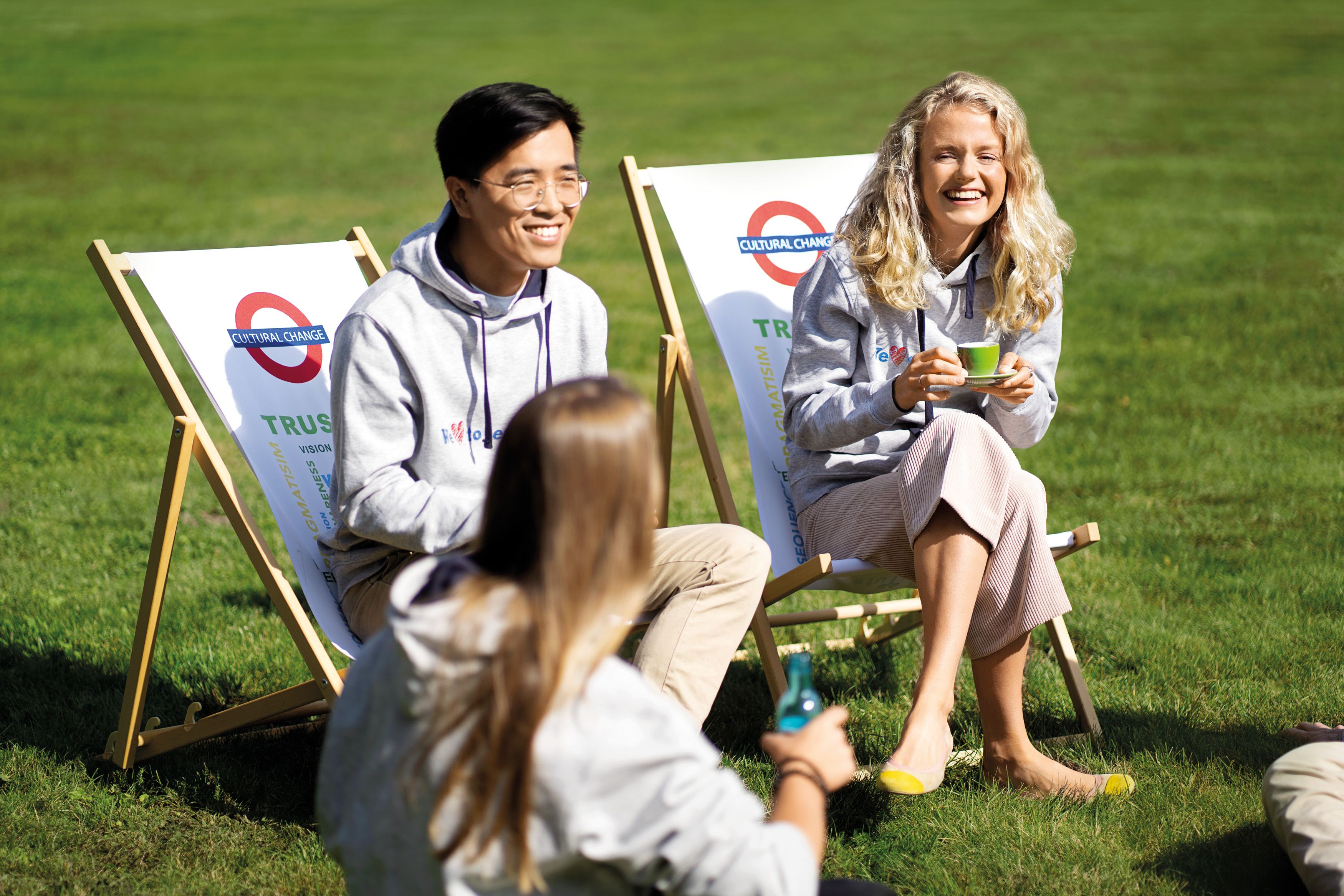 Several employees sit on chairs in the sun while talking with each other.